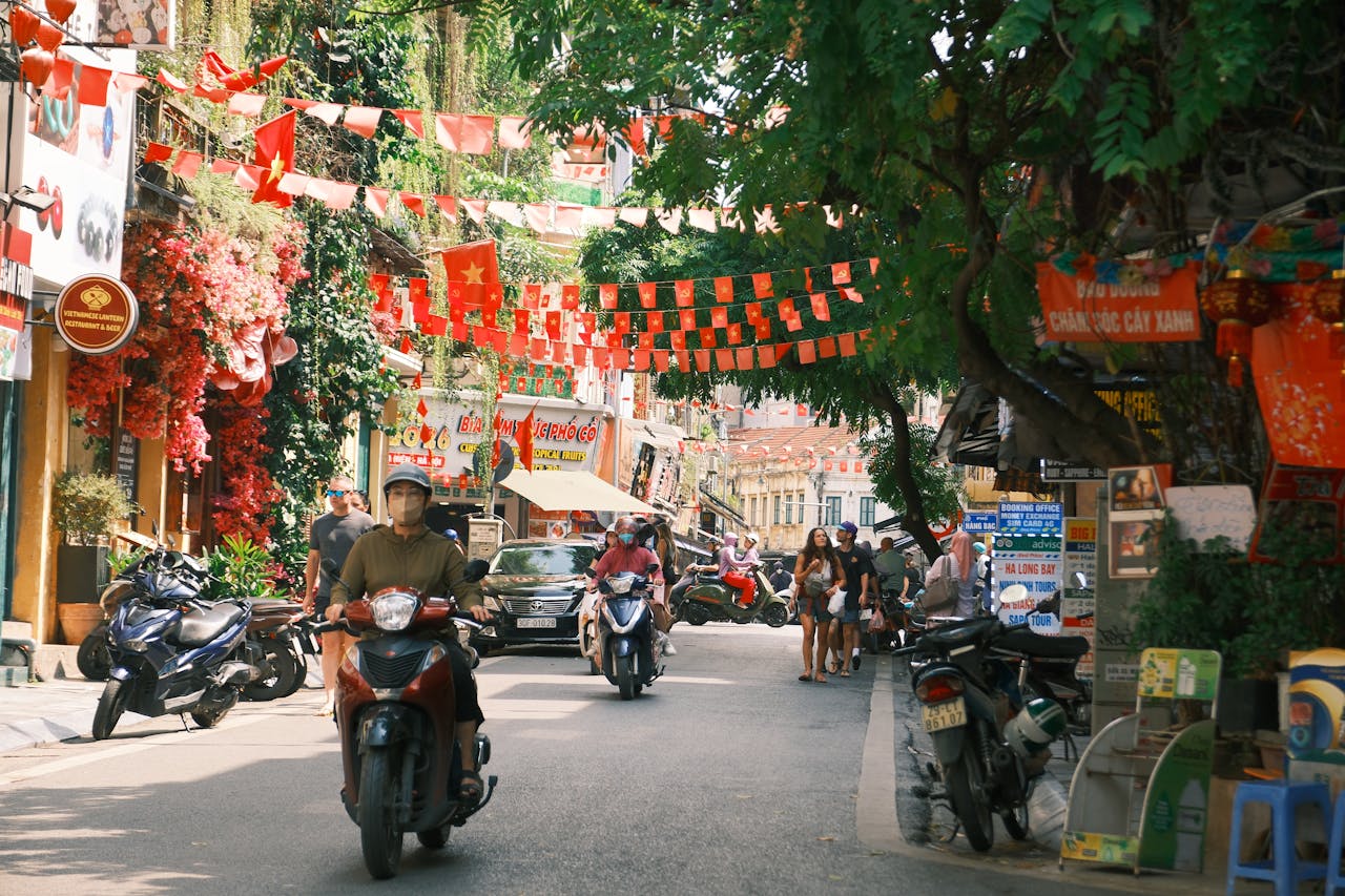 Street scene in Hà Nội featuring locals on motorcycles and colorful decorations.